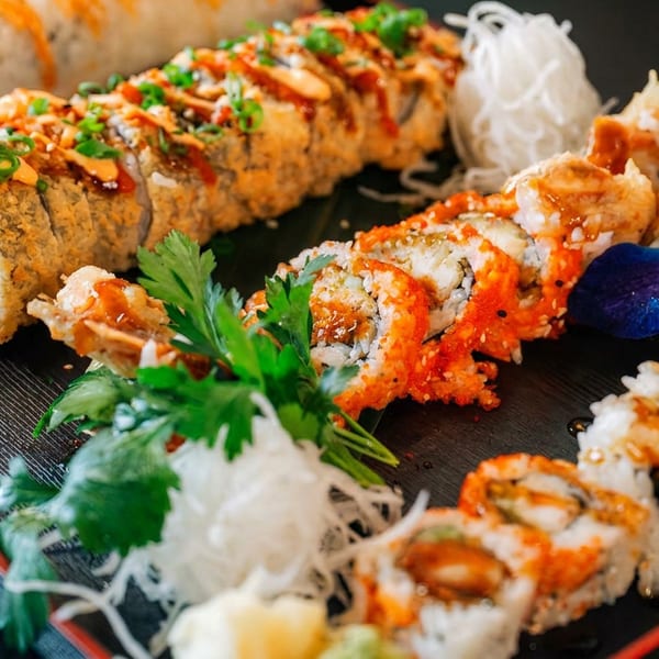 Platter of diverse sushi rolls, including fried and roe-covered, garnished with herbs and orchids.