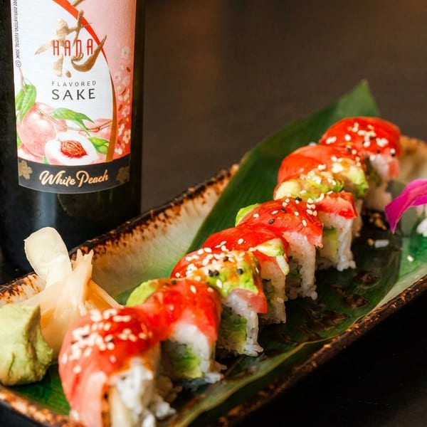Colorful dragon roll sushi with ginger, wasabi, and a bottle of white peach flavored sake.