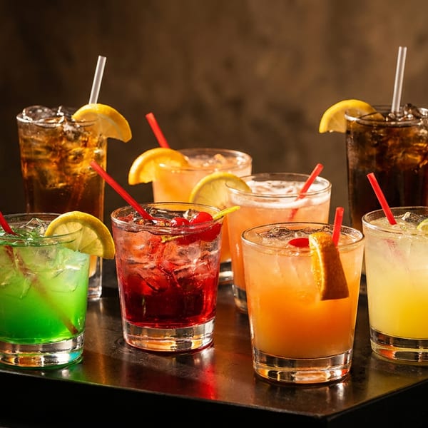 A vibrant assortment of colorful cocktails with fruit garnishes and straws on a dark tray.