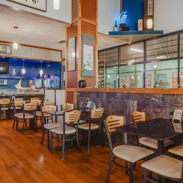 Modern Japanese restaurant interior with dining tables, sushi bar, and blue walls with traditional decor.