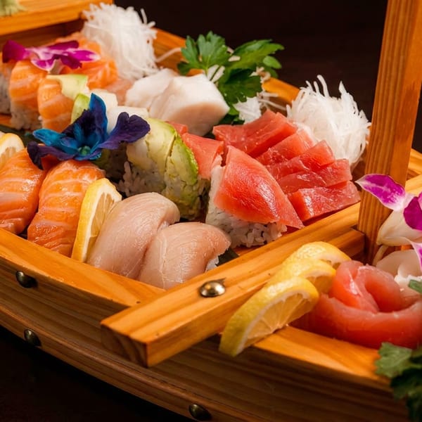 Assorted sushi and sashimi beautifully arranged in a wooden boat, garnished with lemon and flowers.