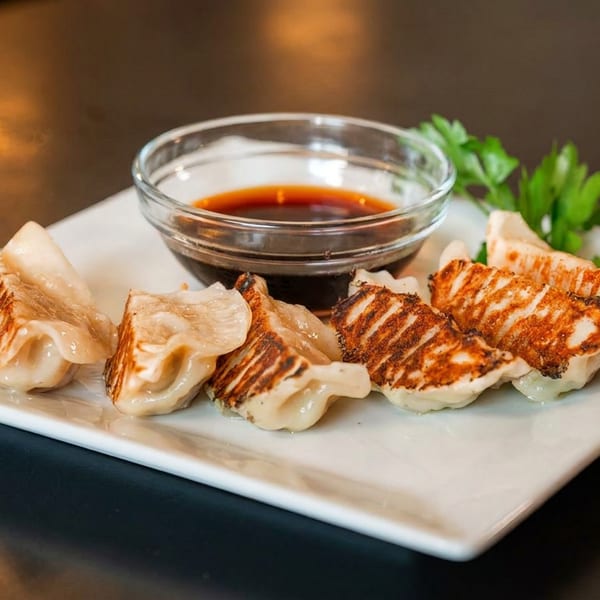 Pan-fried dumplings with crispy bottoms, dipping sauce, and parsley on a white plate.
